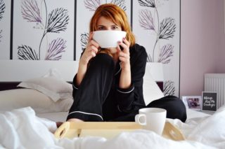 Junge Frau im Pijama auf dem Bett mit einer Tasse in der Hand